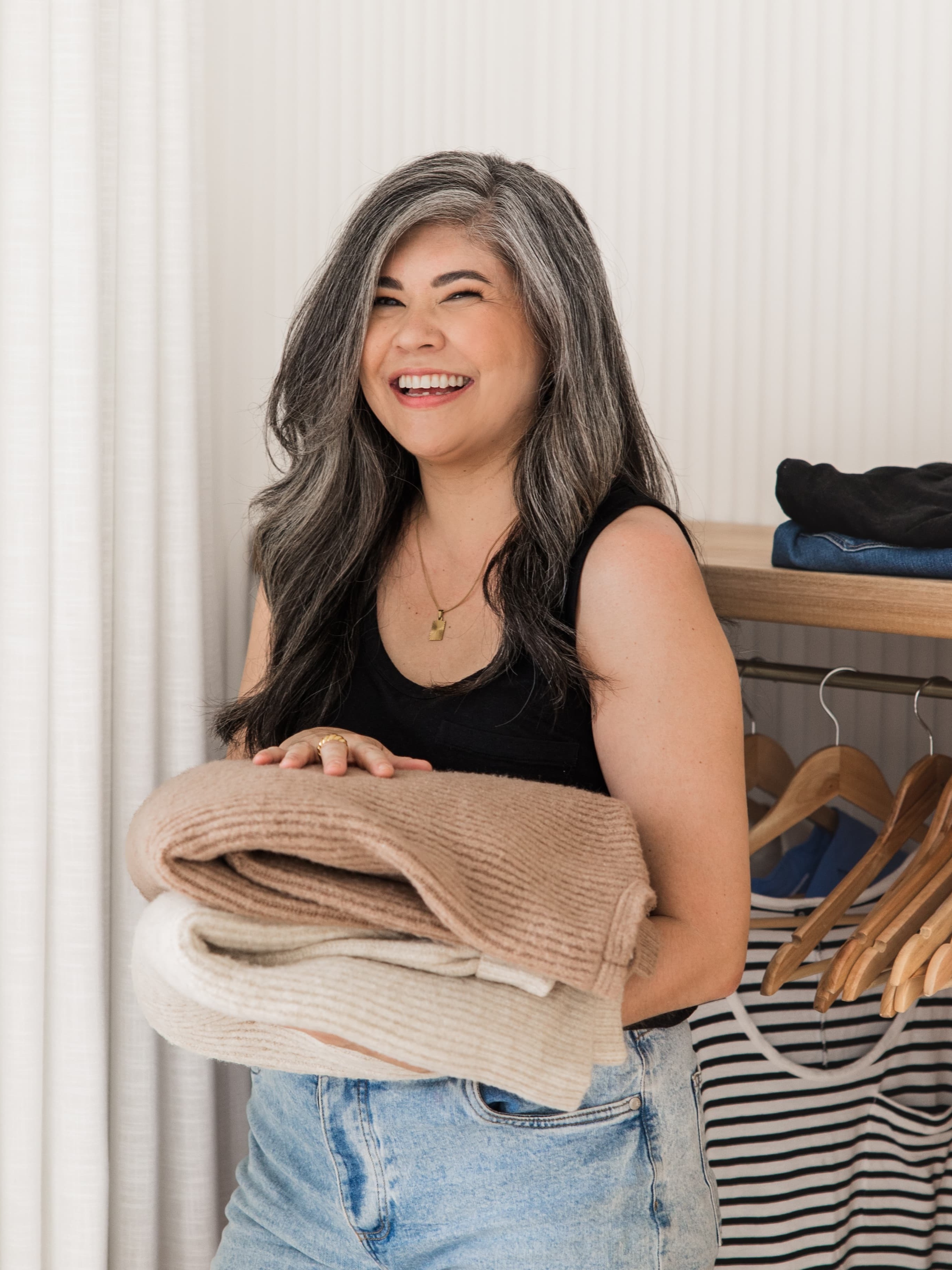 Jennifer from Simply + Fiercely smiling and holding a pile of sweaters